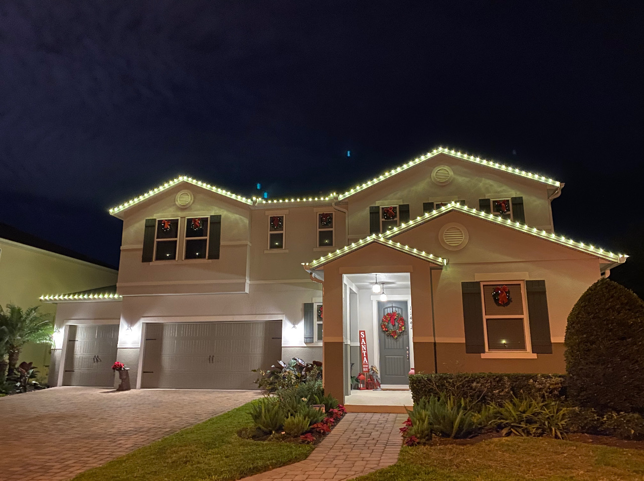 Two-story home outlined in warm white Christmas lights with wreaths on the windows